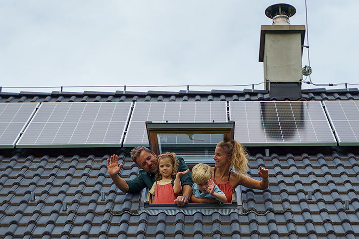Familia asomándose por la ventana de techo de su vivienda, donde tienen placas solares